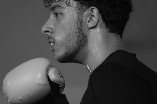 Close-up black and white portrait of a focused male boxer with gloves during training.