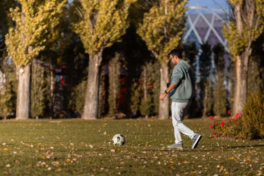 A young man walking in a park beside a soccer ball on a sunny day in Eskişehir, Türkiye.