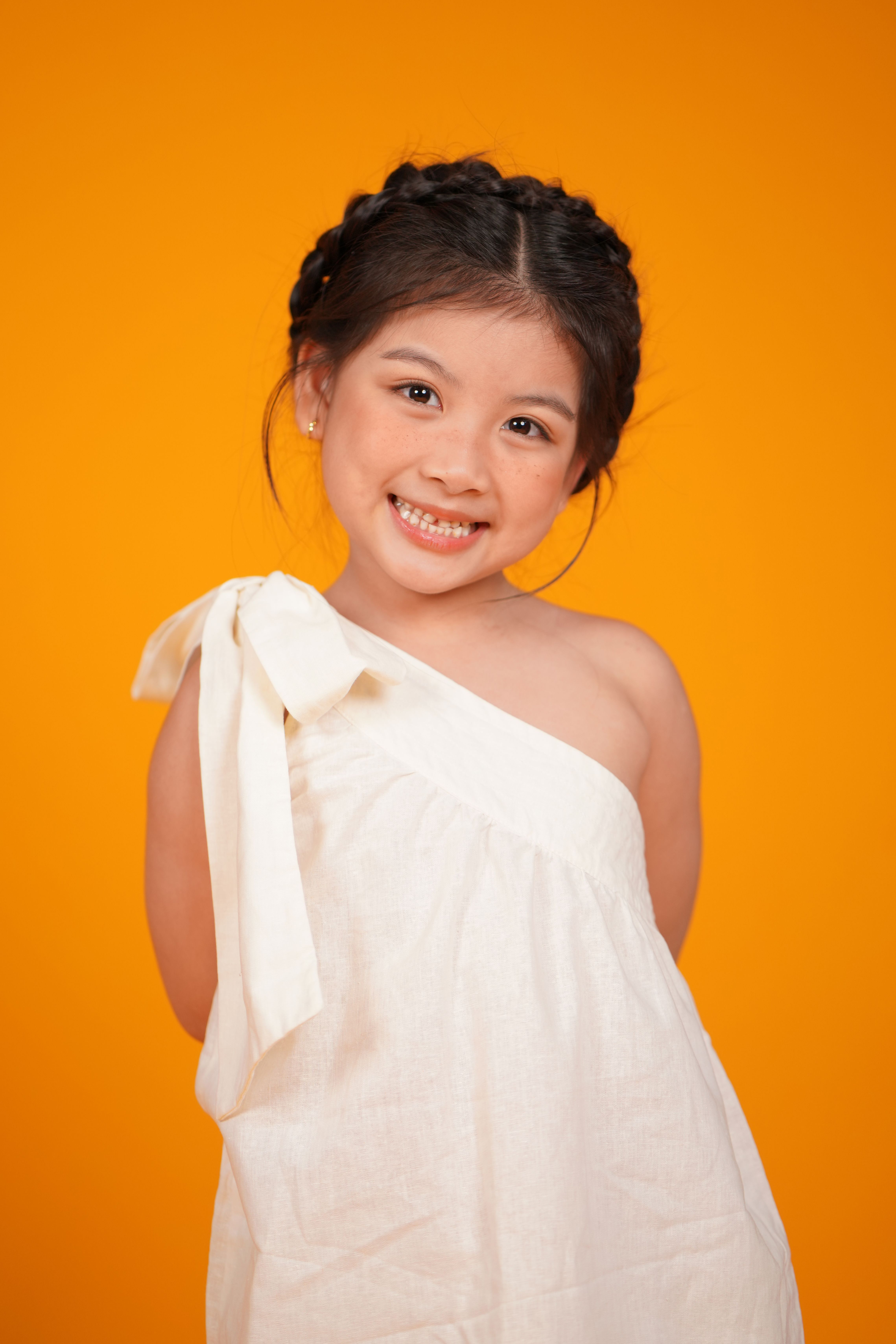 Portrait of a young girl smiling in a white dress with an orange backdrop.