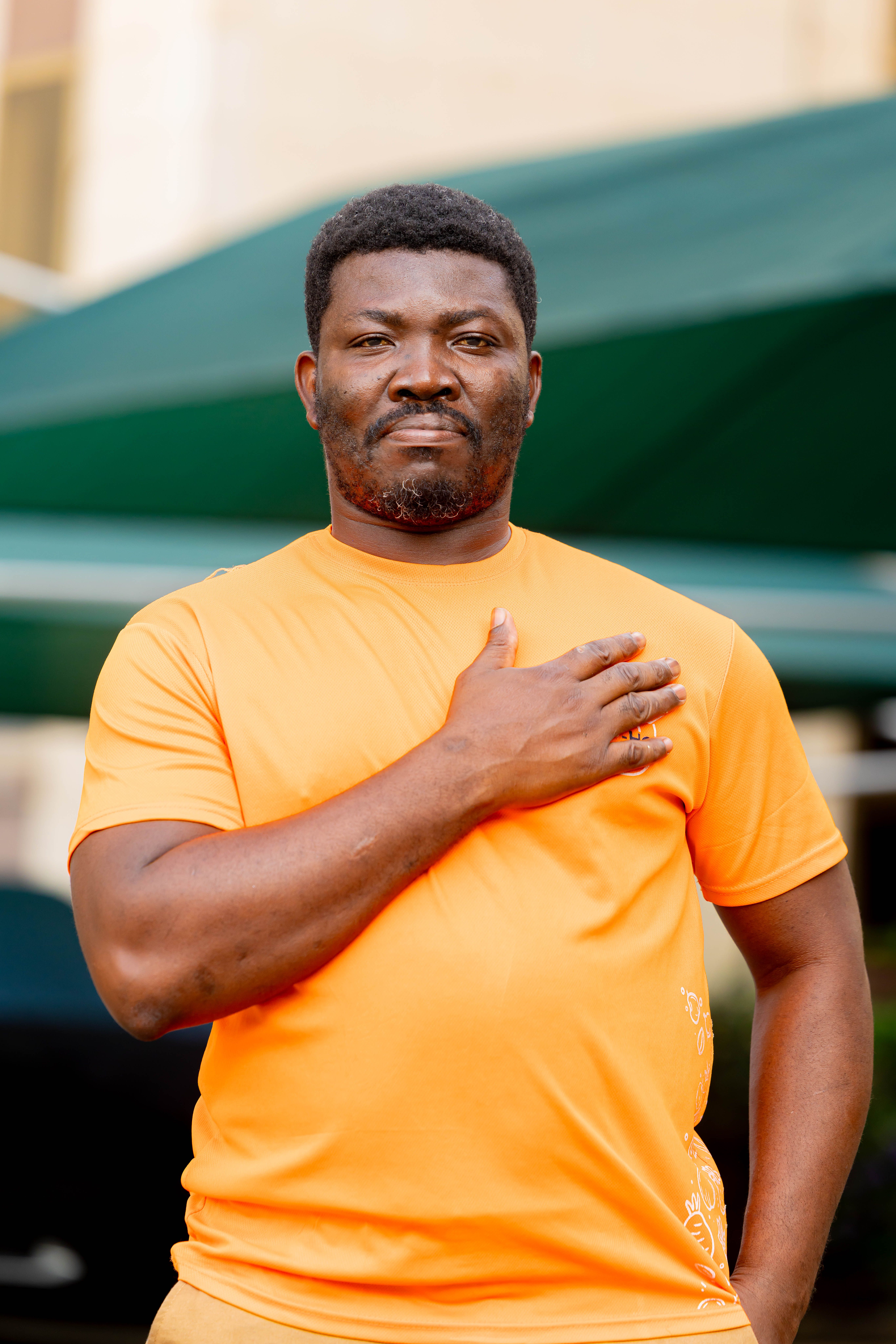 Portrait of a confident man outdoors in casual orange t-shirt posing with hand on chest.