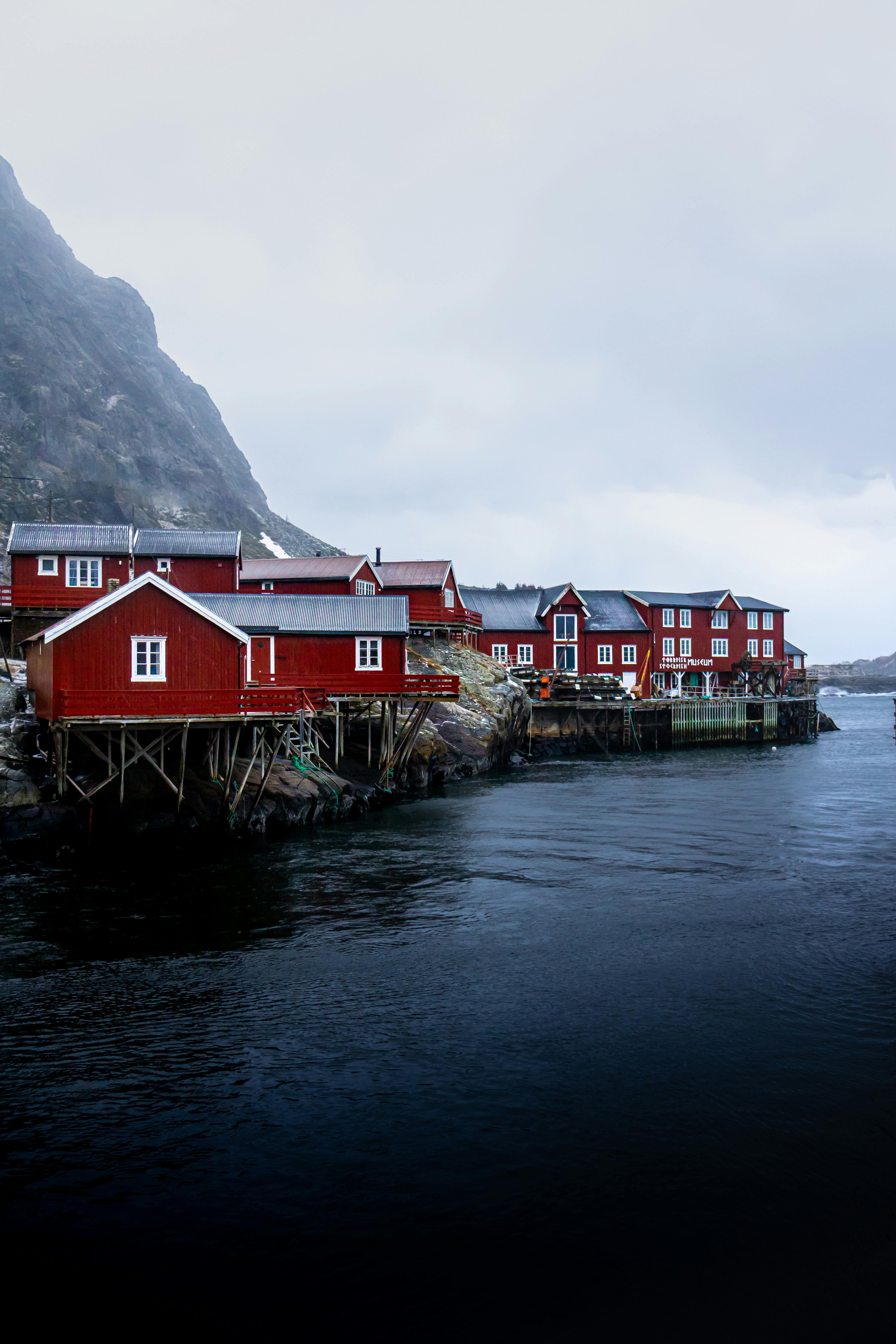 Picturesque red cabins on stilts beside the calm fjord, capturing Norway's serene coastal beauty.
