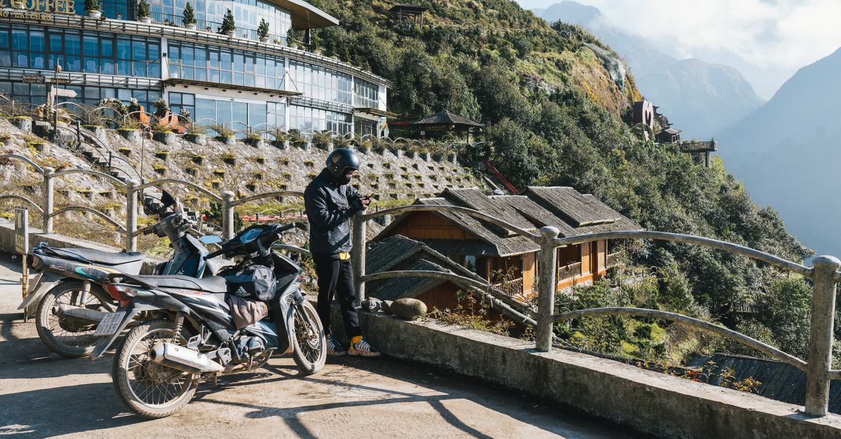 A traveler with motorbikes at a scenic café in Sapa, Vietnam, enjoying sunny mountain views.