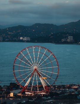 Beautiful ferris wheel at sunset against a lake and mountain backdrop, offering a picturesque view.