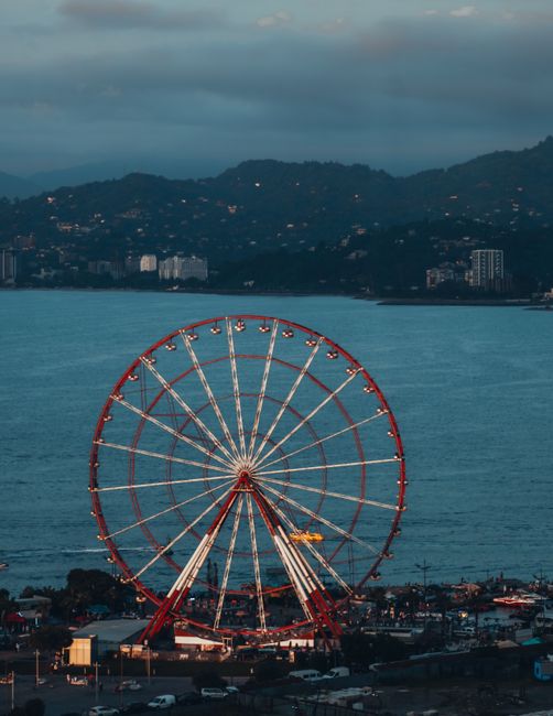 Beautiful ferris wheel at sunset against a lake and mountain backdrop, offering a picturesque view.