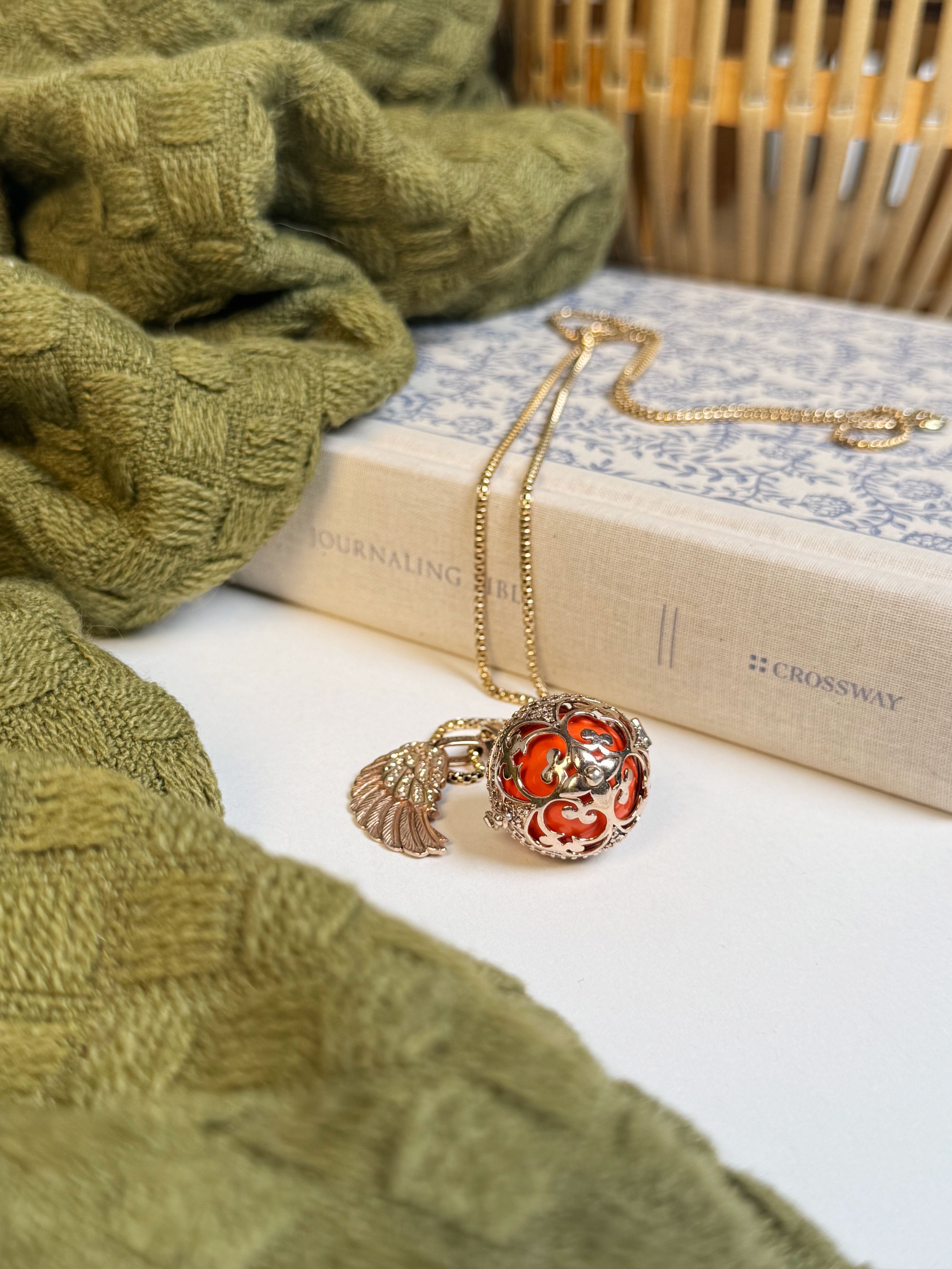 Gold necklace with intricate pendant resting on a book, framed by cozy green fabric.