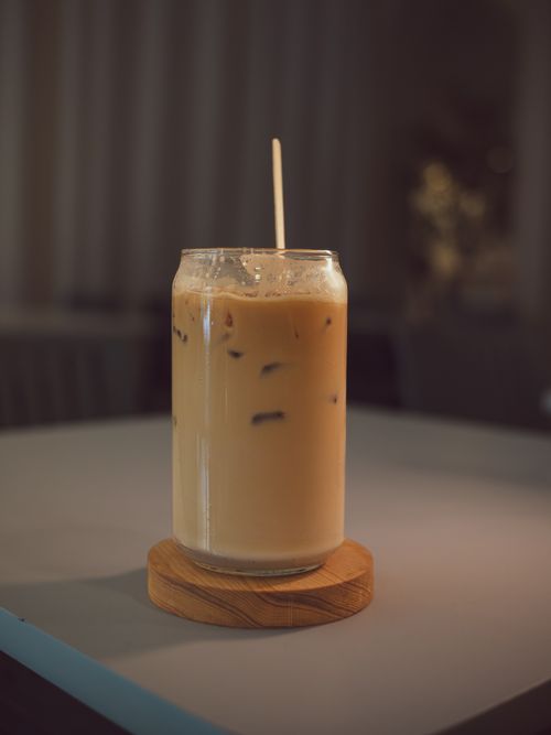 Free A close-up shot of an iced coffee with a straw on a wooden coaster in ambient lighting. Stock Photo