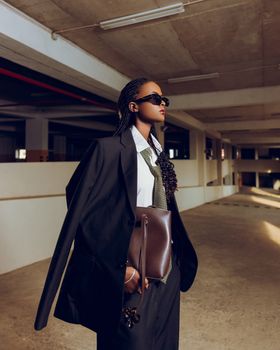 Stylish woman in a suit and sunglasses, in a modern urban environment, exuding confidence.