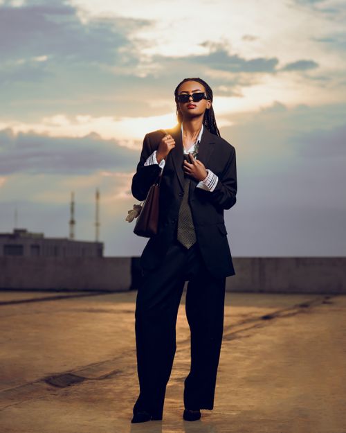 Free Confident woman in suit and sunglasses standing on a rooftop at sunset. Stock Photo