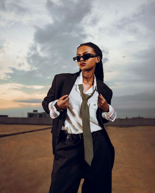 Free Stylish woman in suit and tie poses confidently at sunset against urban backdrop. Stock Photo
