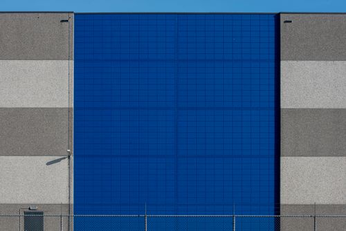 Free Photo of a modern industrial building showcasing a vibrant blue facade contrasted with neutral tones. Stock Photo