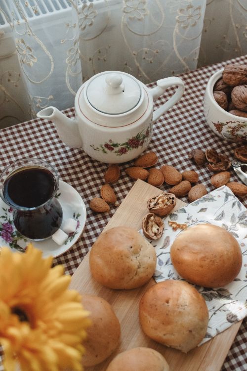 Free A cozy afternoon tea setup featuring fresh buns, mixed nuts, and a floral teapot on a gingham tablecloth. Stock Photo