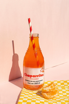 Tasty Chaparritas orange soda with citrus slices on a pink background.