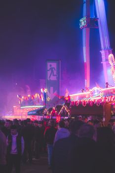 Colorful nighttime scene at a bustling fairground with festive lights and a lively crowd.