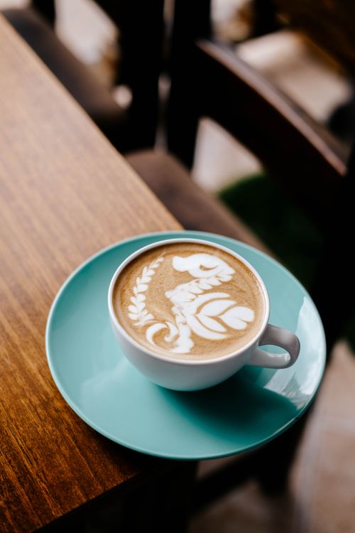 Free Beautiful coffee latte with intricate latte art served in an aqua cup on a wooden table. Stock Photo