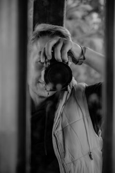 Monochrome image of a photographer capturing a shot through a window reflection.