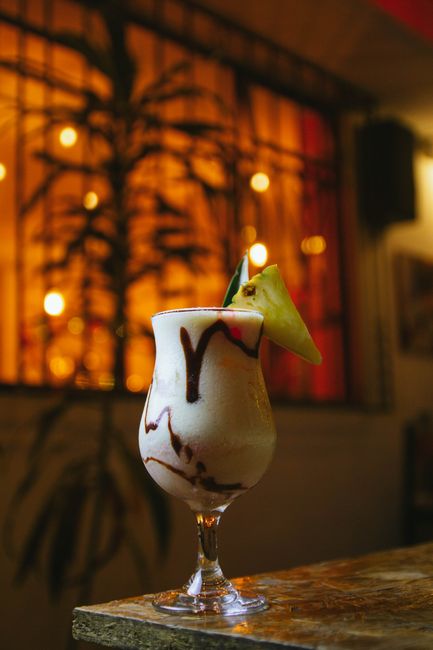 A tall glass of orange-red Bahama Mama cocktail layered with grenadine at the bottom, garnished with a pineapple wedge and maraschino cherry on a bamboo skewer.