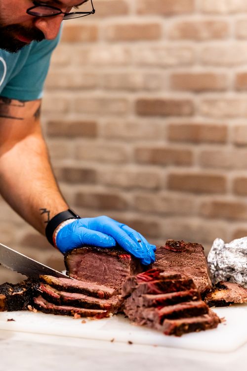Free Chef with glove slicing tender smoked beef brisket on a white cutting board indoors. Stock Photo