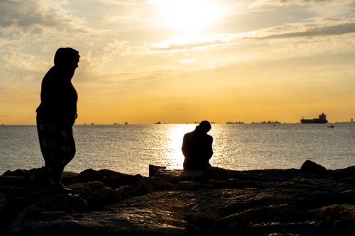 Free Silhouettes of two individuals on rocks by the sea during a tranquil sunset. Stock Photo