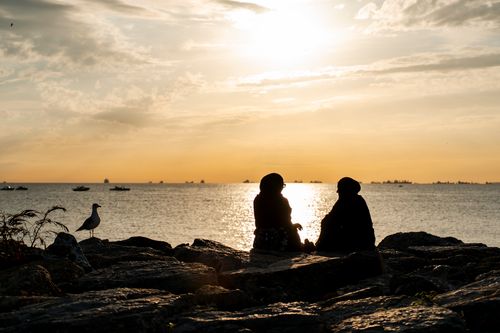 Free Two people silhouetted against a vibrant sunset by the sea, creating a serene atmosphere. Stock Photo