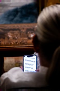 A woman reads a smartphone in a dimly lit setting with focus on screen text.