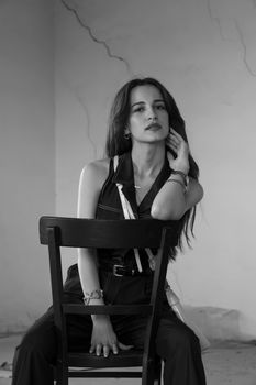 Elegant black and white portrait of a woman seated on a chair in a minimalist setting.