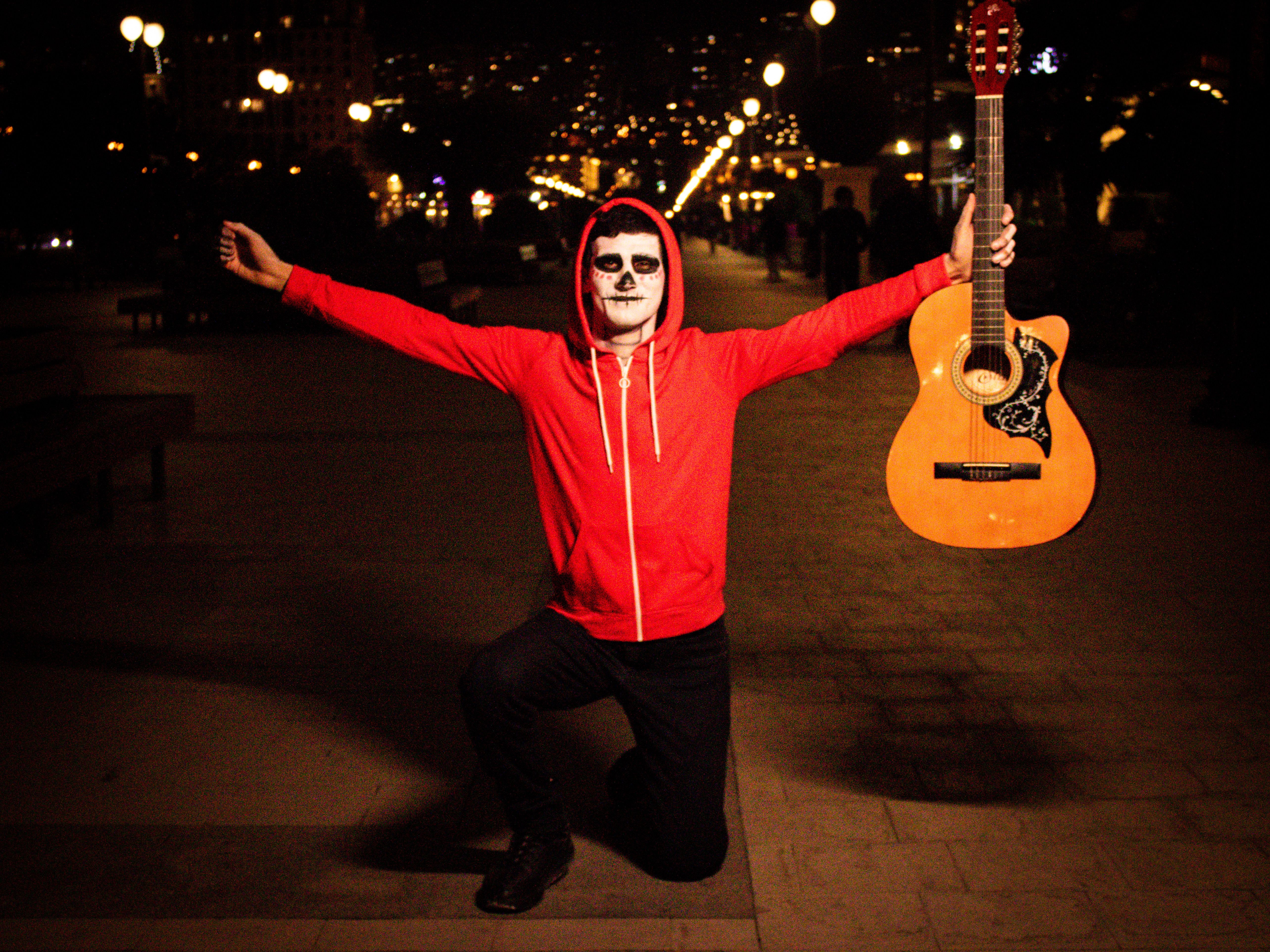 A performer in makeup holding a guitar at night; festive and lively atmosphere.