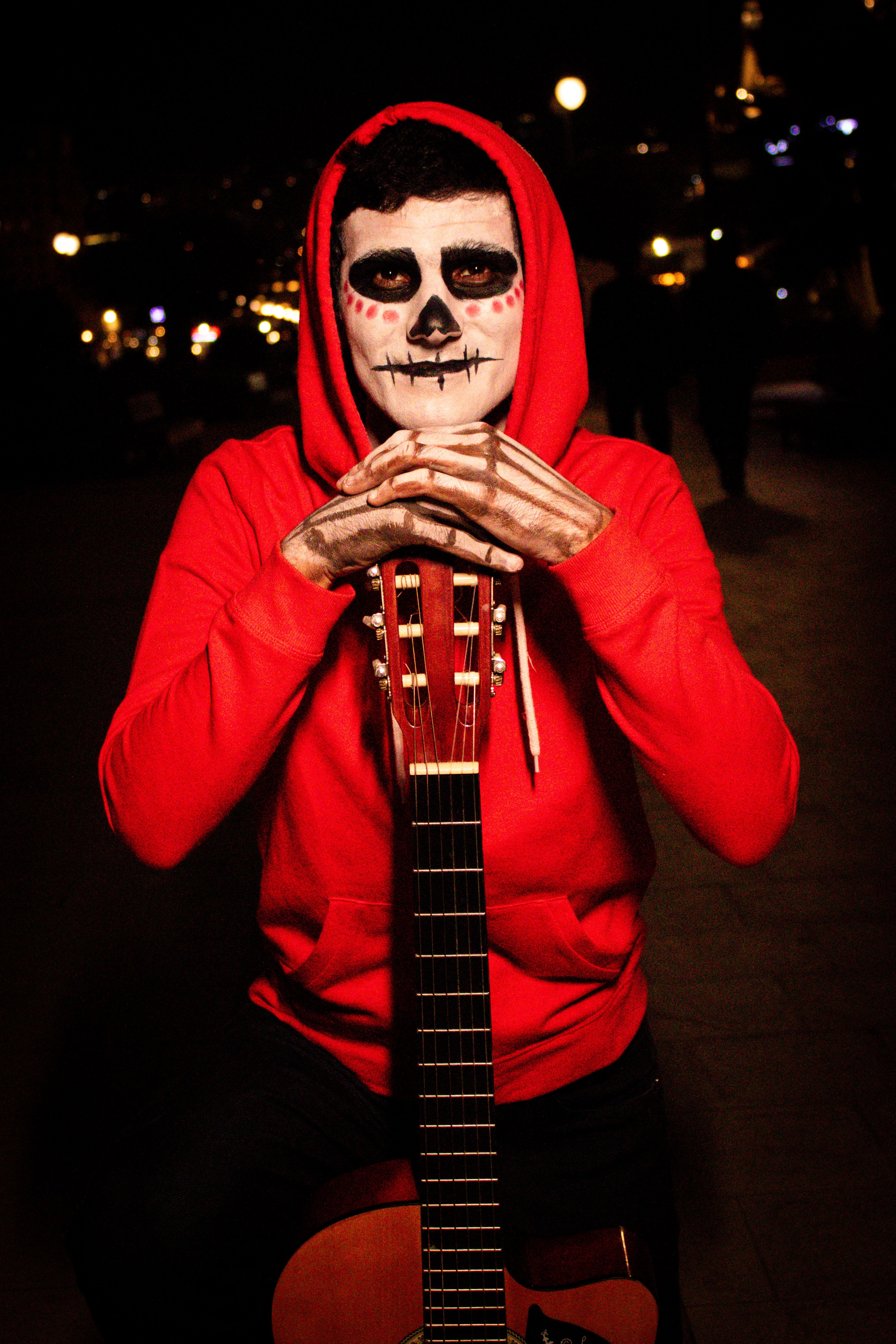 Person with skeleton makeup and a guitar at night, evoking Day of the Dead.
