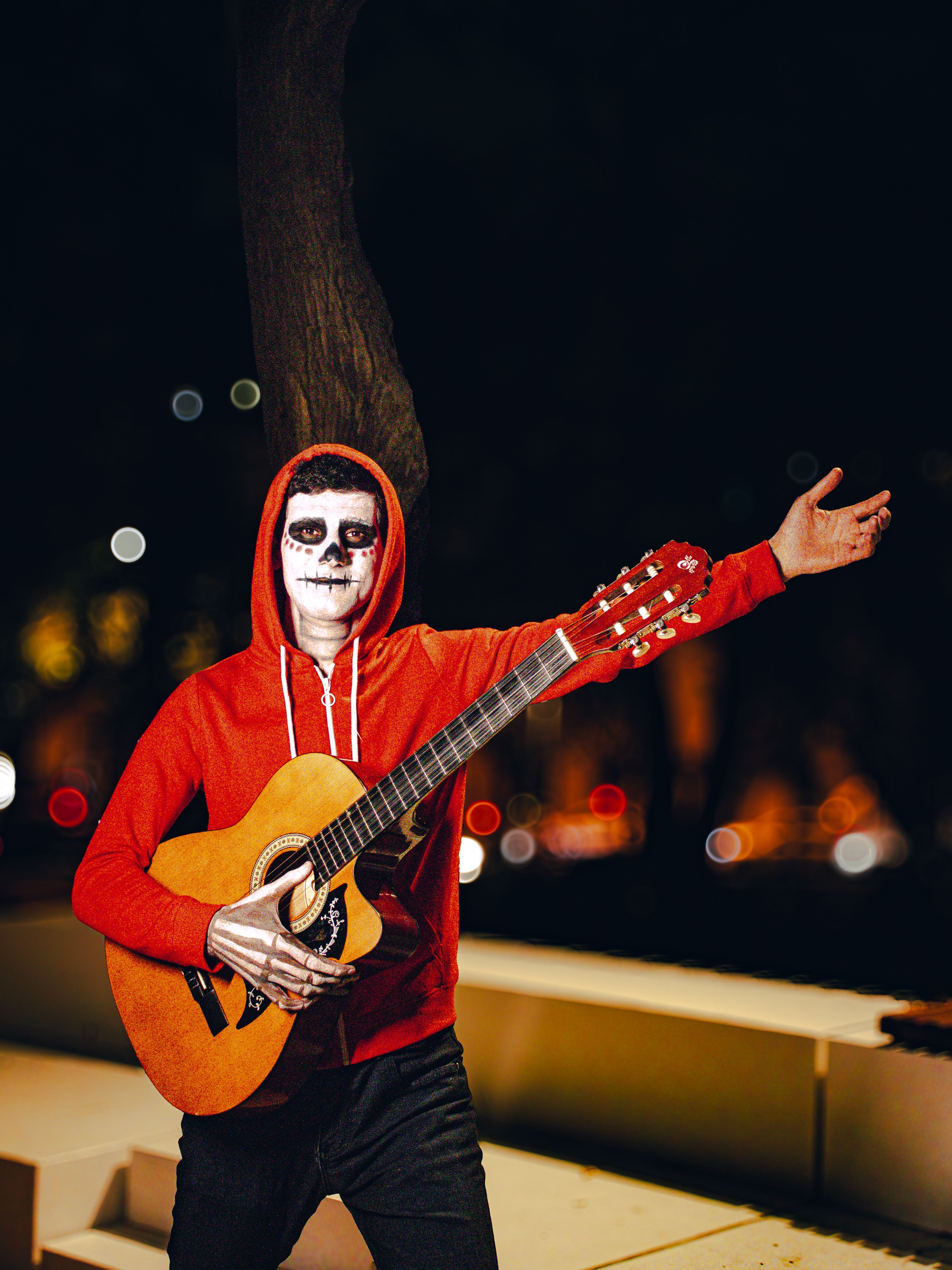 Man with face paint and guitar posing outdoors at night during Halloween.