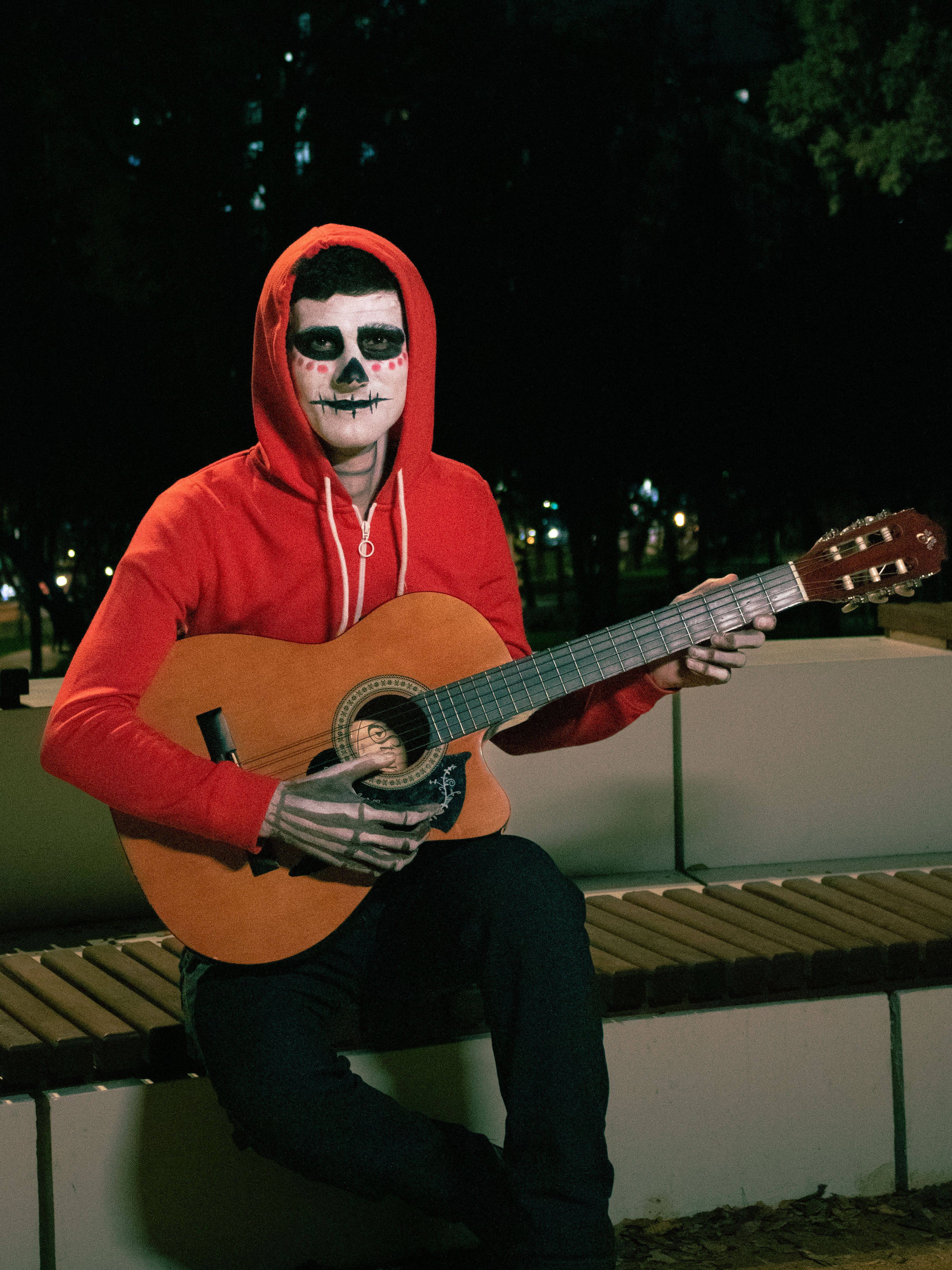 A person in skeleton makeup strums a guitar at night, embodying a Halloween theme.