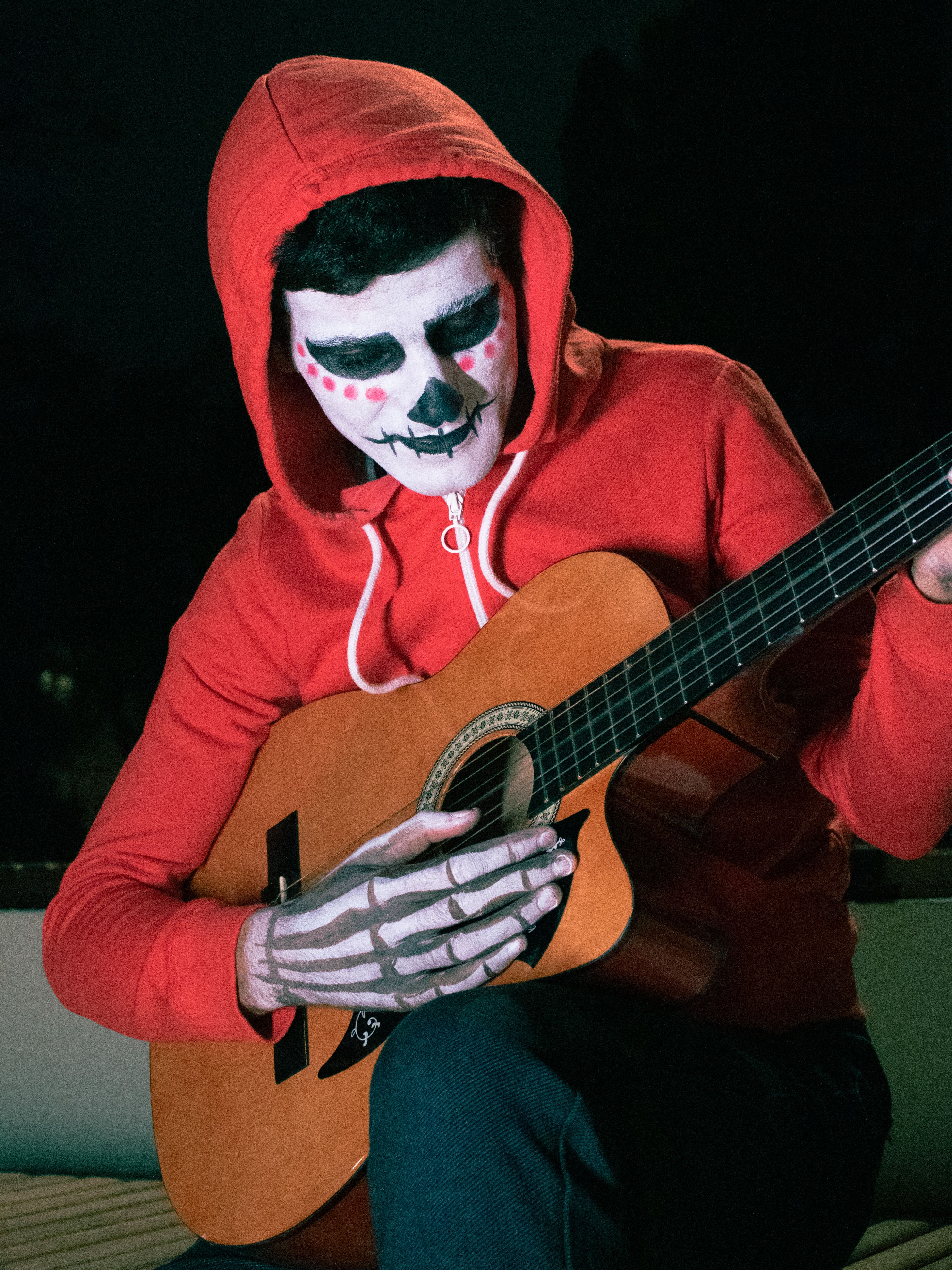 A person in Day of the Dead makeup playing guitar during nighttime.