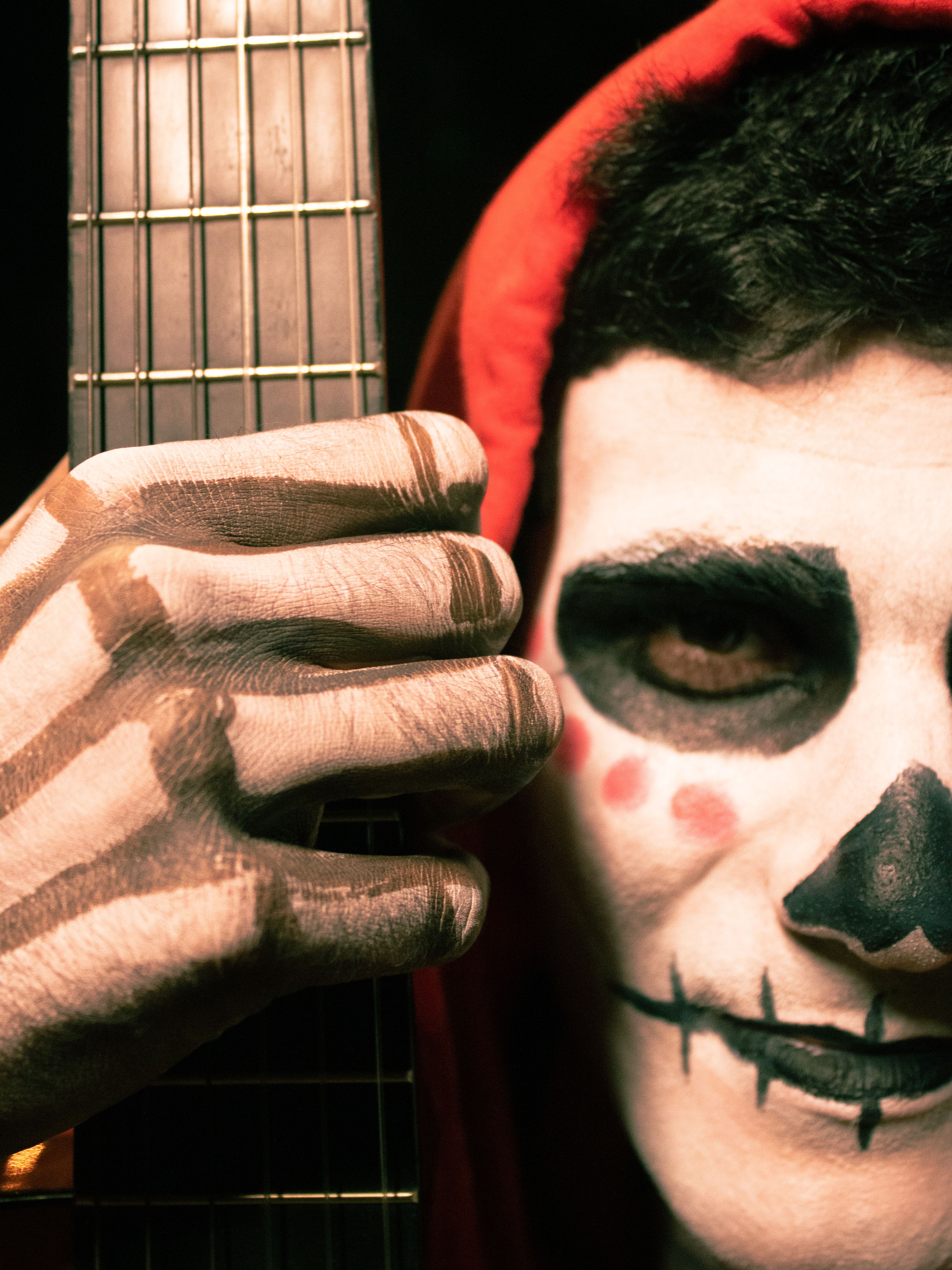 Skull makeup on a person's face holding a guitar, creating a spooky Halloween vibe.