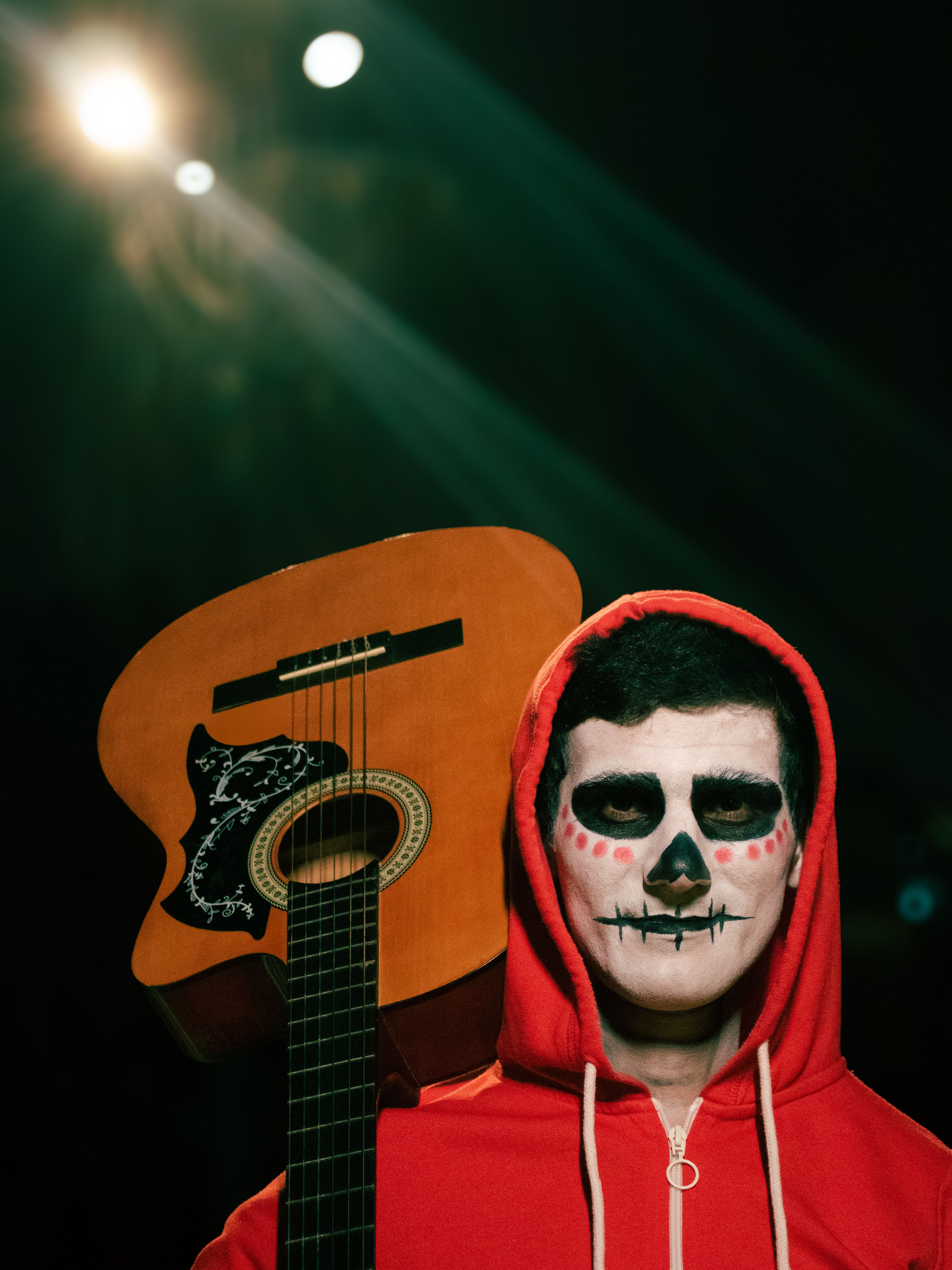 A person with face paint holds a guitar under dramatic lighting in a dark setting.