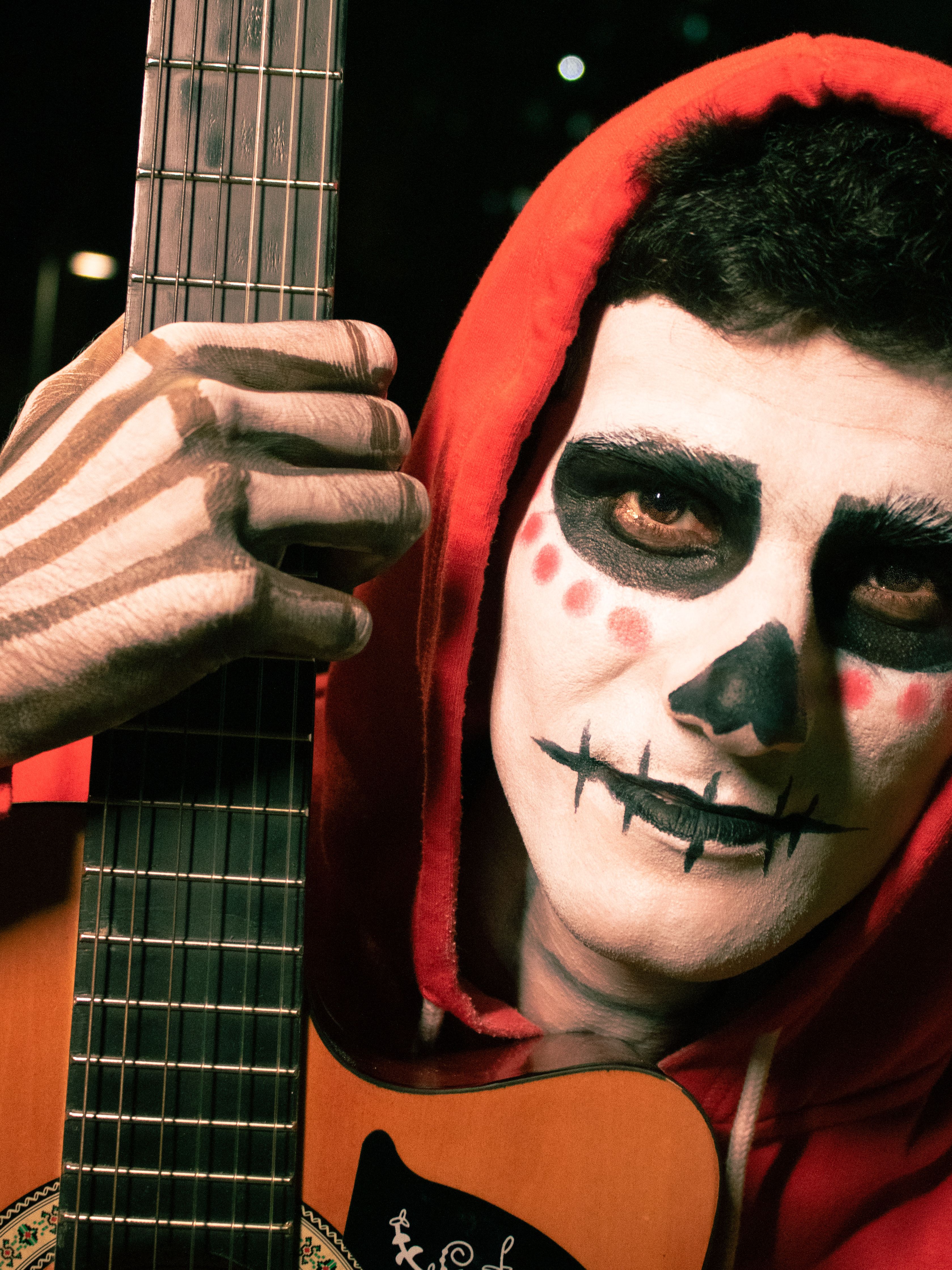 Man in skeleton makeup and red hoodie holds guitar, exuding vibrant festive spirit.