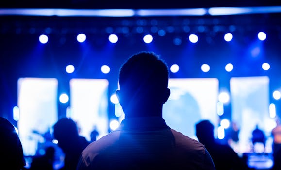Back view of audience members enjoying a live concert with blue stage lighting.