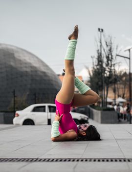Woman in vibrant yoga pose on urban street wearing pink bodysuit.