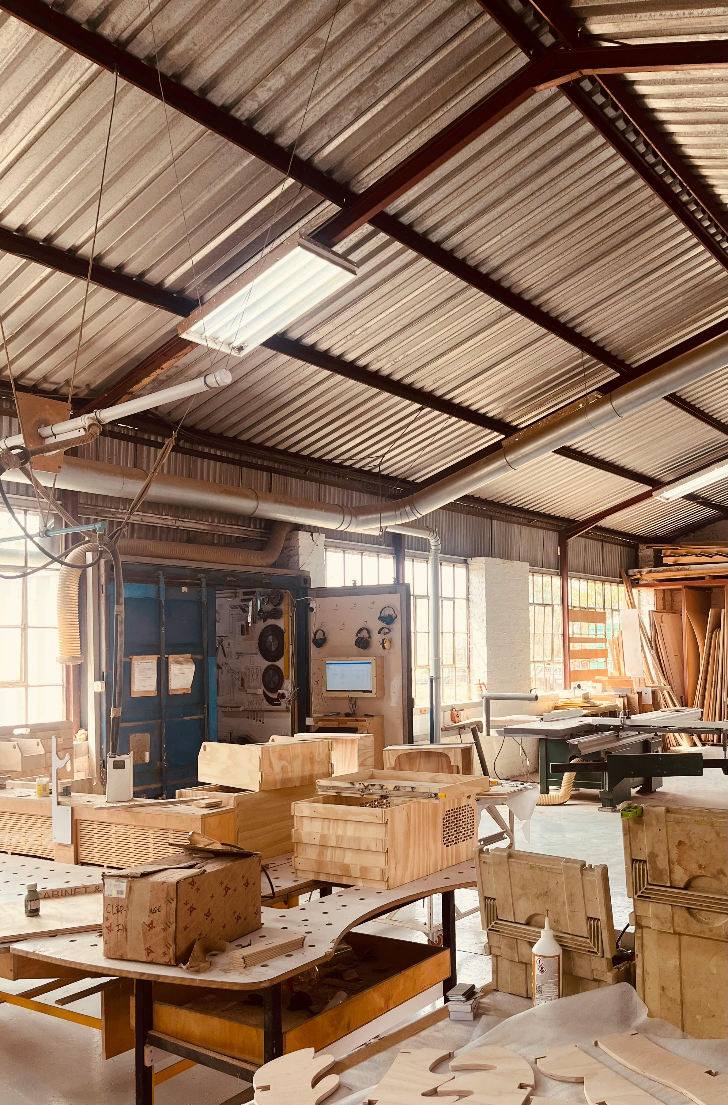 Workshop interior with wooden projects on tables, under a corrugated metal roof.