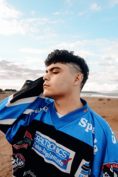Free A young man wearing a vibrant jersey poses on a beach under a cloudy sky. Stock Photo