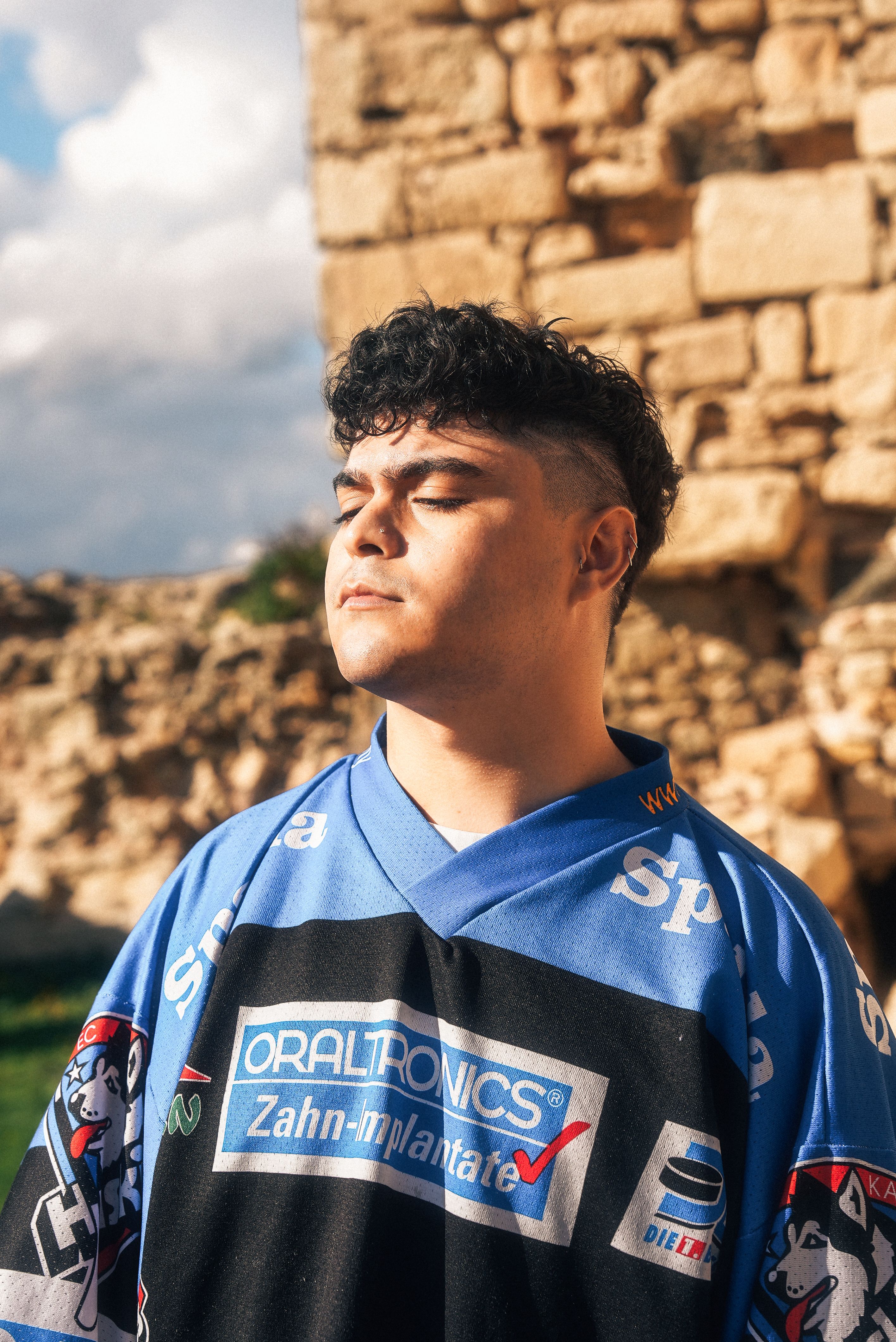 Portrait of a young man in a blue jersey with eyes closed, enjoying sunlight.