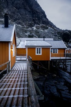 Snow-dusted Nordic cabins under a rugged mountainside at dusk, showcasing rustic charm.
