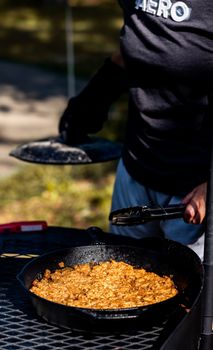 Person cooking outdoors with a cast iron skillet filled with seasoned food, perfect for camping