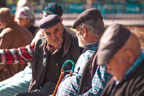 Free A group of senior men with hats talk and relax on a sunny day, showcasing warmth and friendship. Stock Photo