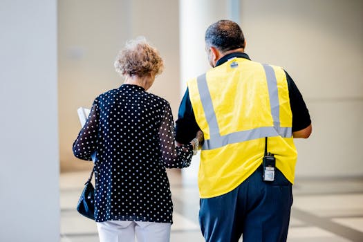 A security officer helps an elderly woman inside a modern building hallway.