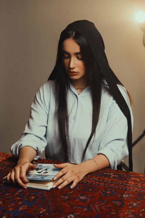 Free A young woman in contemplative thought, holding a book with a serene expression. Stock Photo