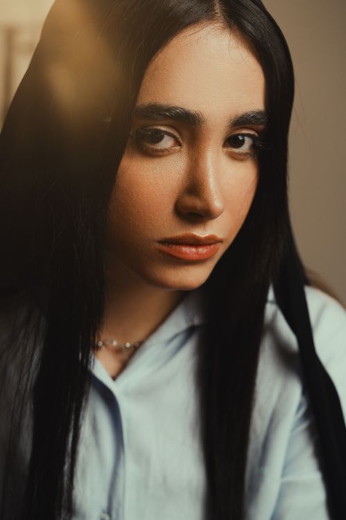 Free Close-up portrait of a young woman with long black hair and intense gaze, wearing a light blue shirt. Stock Photo