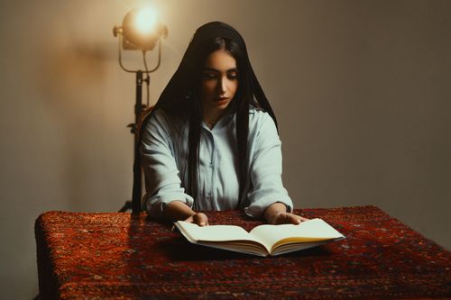 Free A woman in a serene setting reads a book under soft, dramatic lighting. Stock Photo