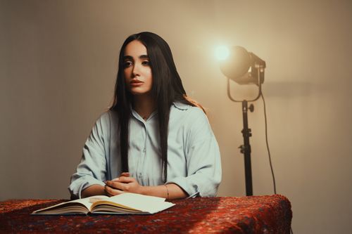 Free Woman sitting at a table with an open book and behind her a studio light Stock Photo