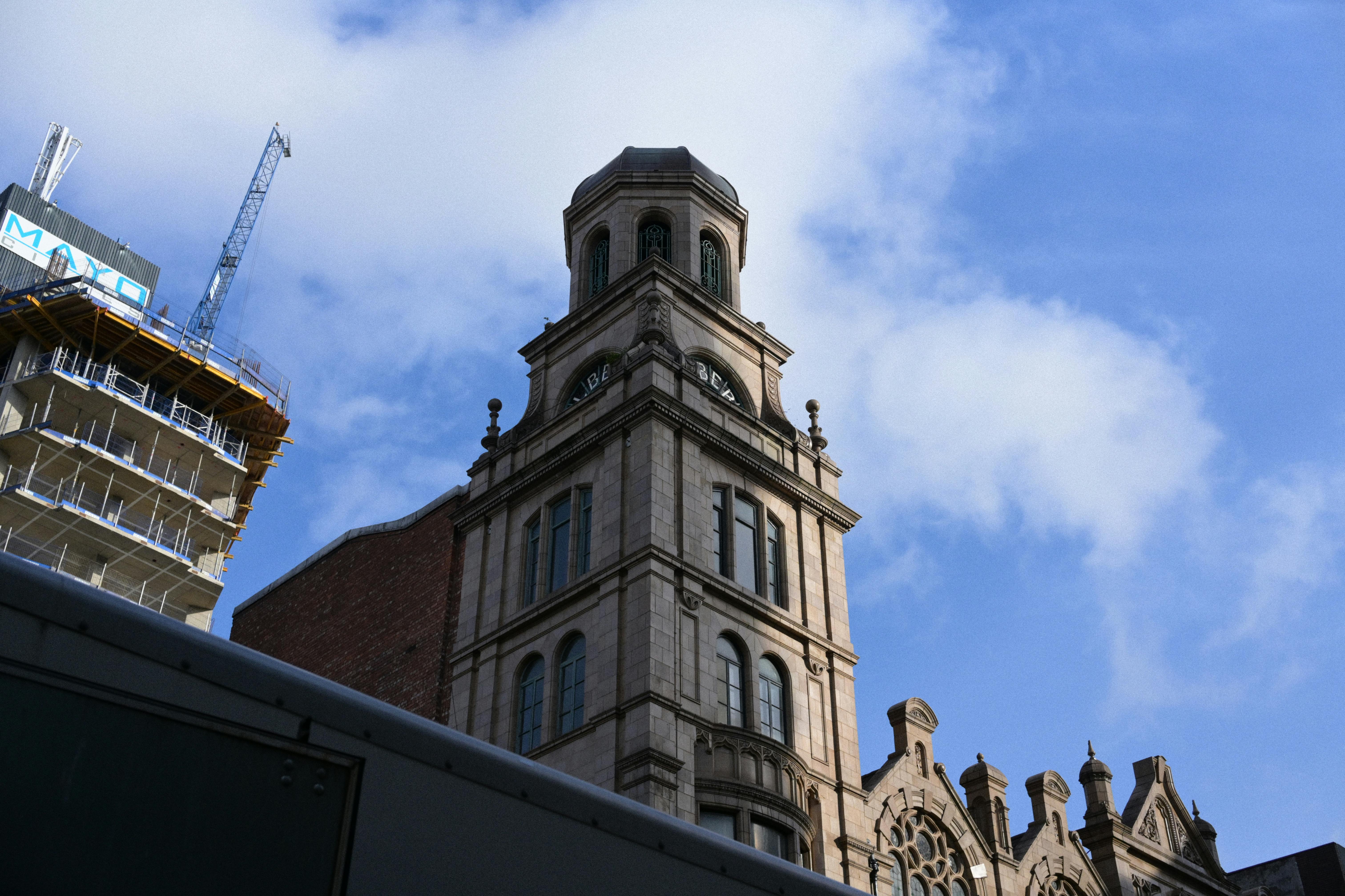 A historic clock tower rises amidst modern construction under a vibrant blue sky.