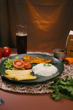 A vibrant Brazilian meal featuring fish, rice, salad, and fries on a decorative table setting.