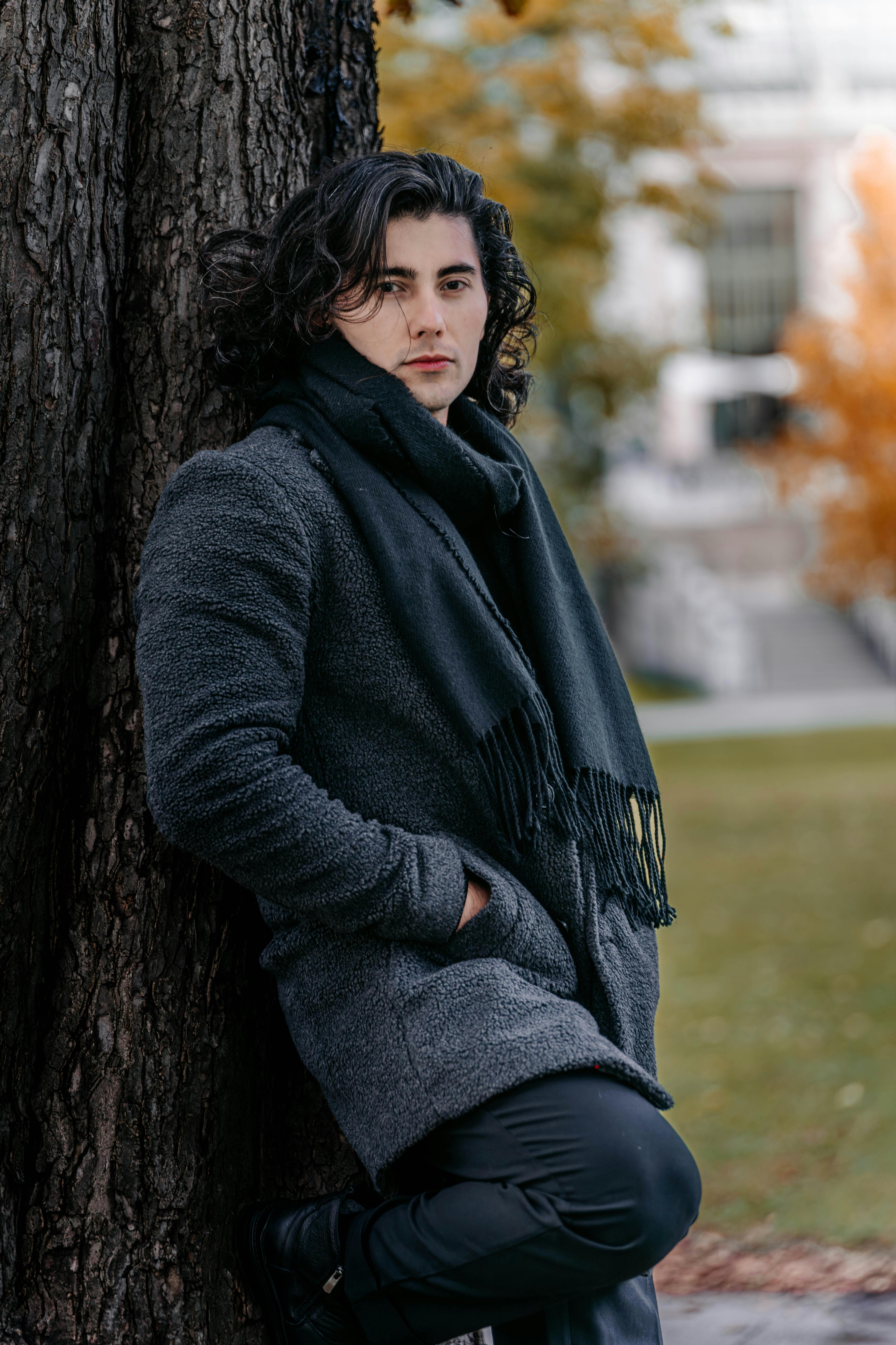 Gratis Model pria elegan dalam busana musim gugur bersandar di pohon dengan latar belakang Wina yang kabur. Foto Stok