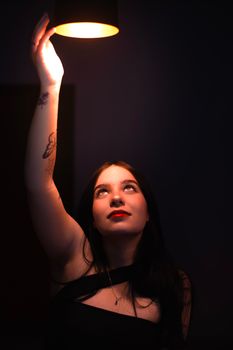 A woman reaches towards a glowing light fixture, creating a dramatic and artistic atmosphere.